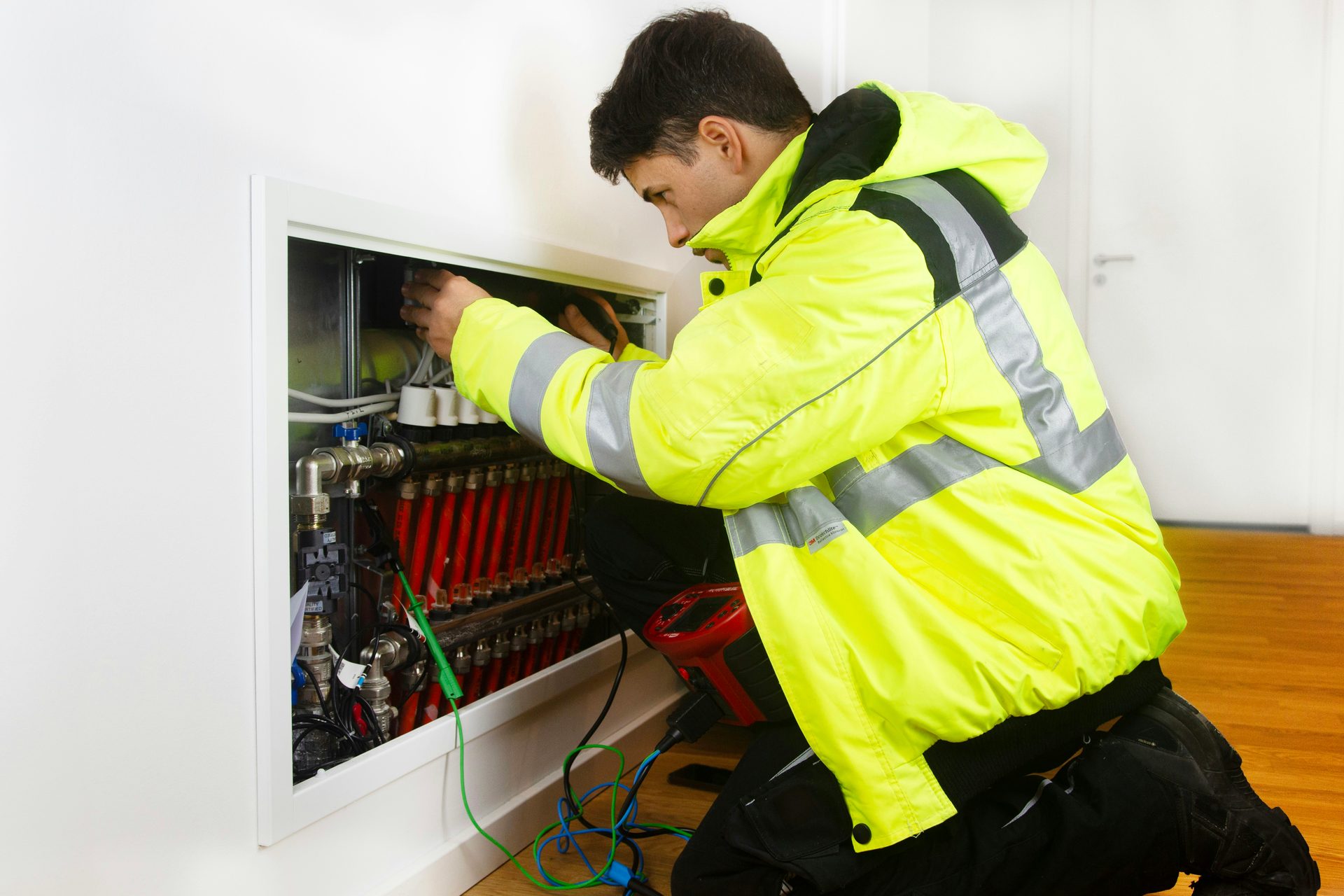 An electrician in a yellow high-visibility jacket working at an open household switchboard.